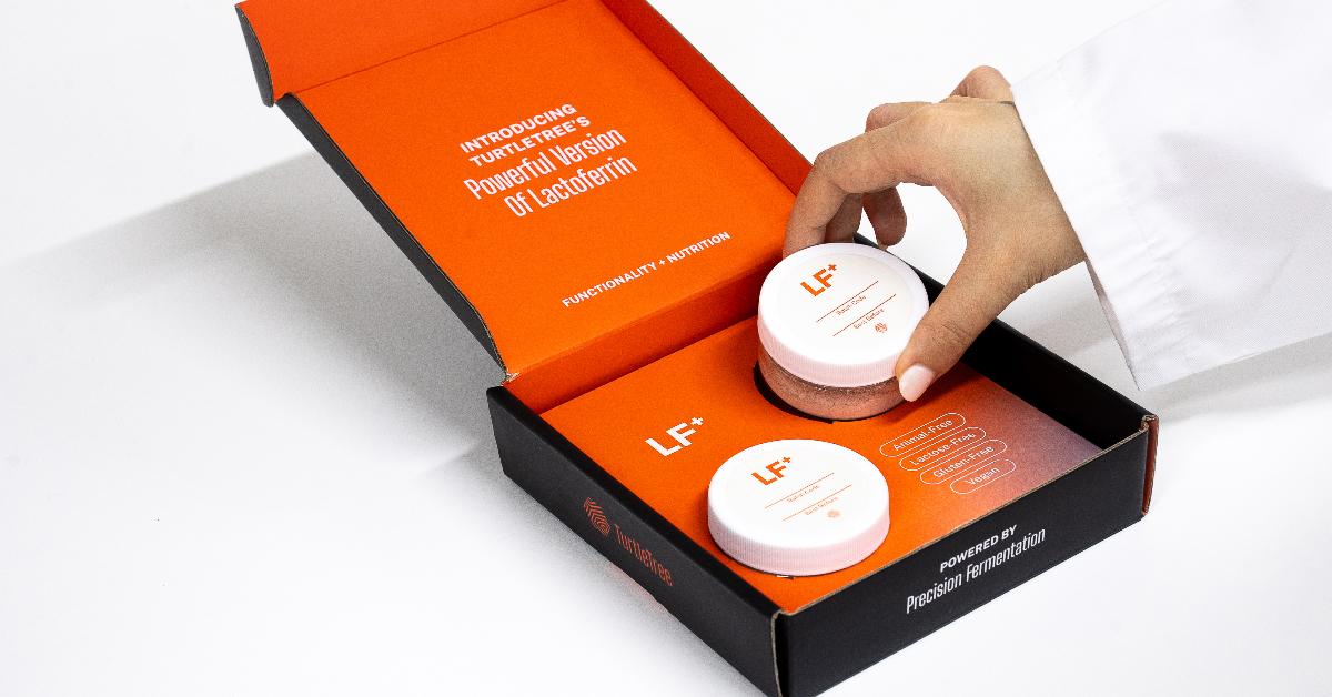 Photo of a hand placing biotech company TurtleTree's vegan lactoferrin product, LF+, in a black and orange box