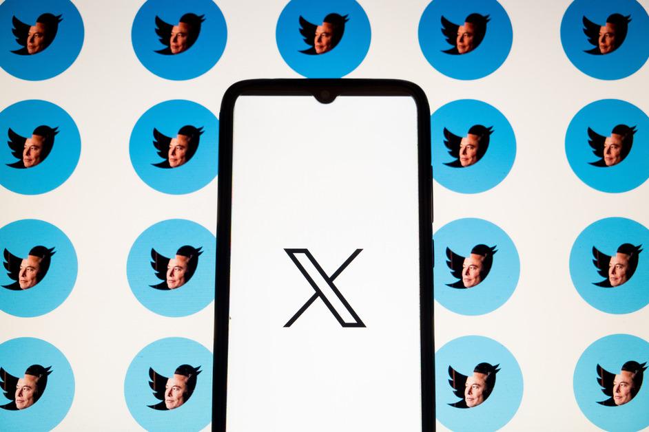 A photo of a phone screen with the X logo on the screen in from of a background of Elon Musk's face filling the Twitter bird logo.